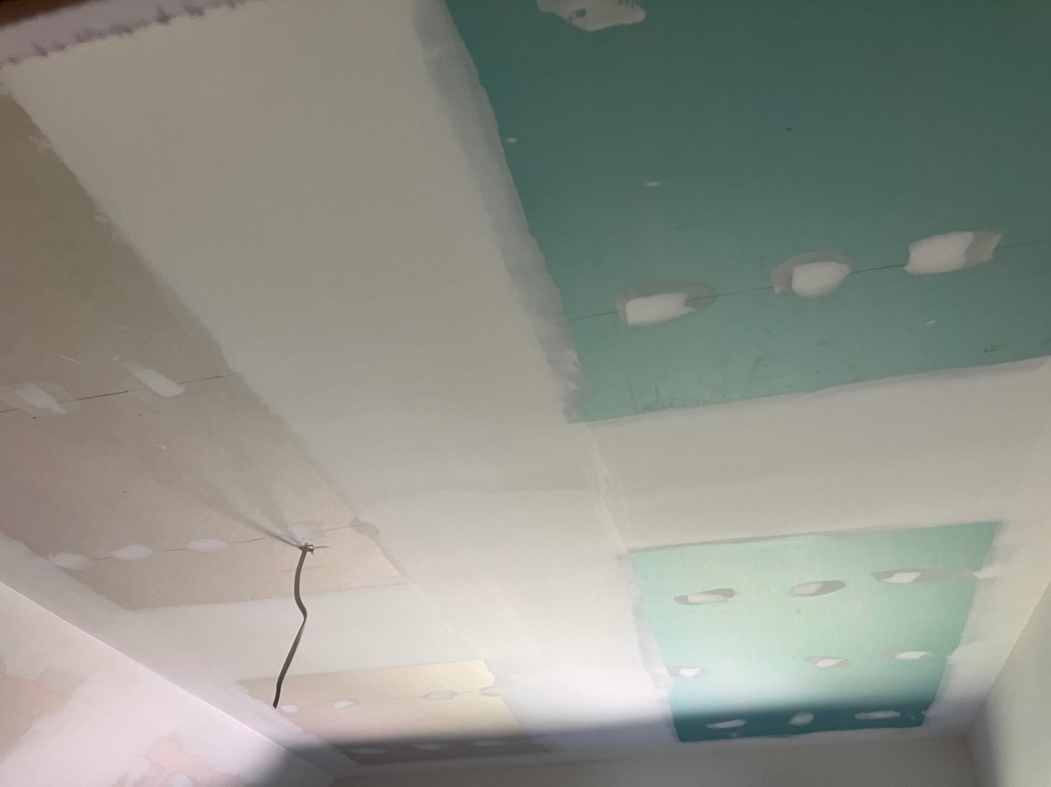 Sufit z płyt gipsowo-kartonowych w trakcie szpachlowania, widoczne łączenia płyt i otwory po wkrętach wypełnione masą szpachlową, wystający kabel elektryczny.