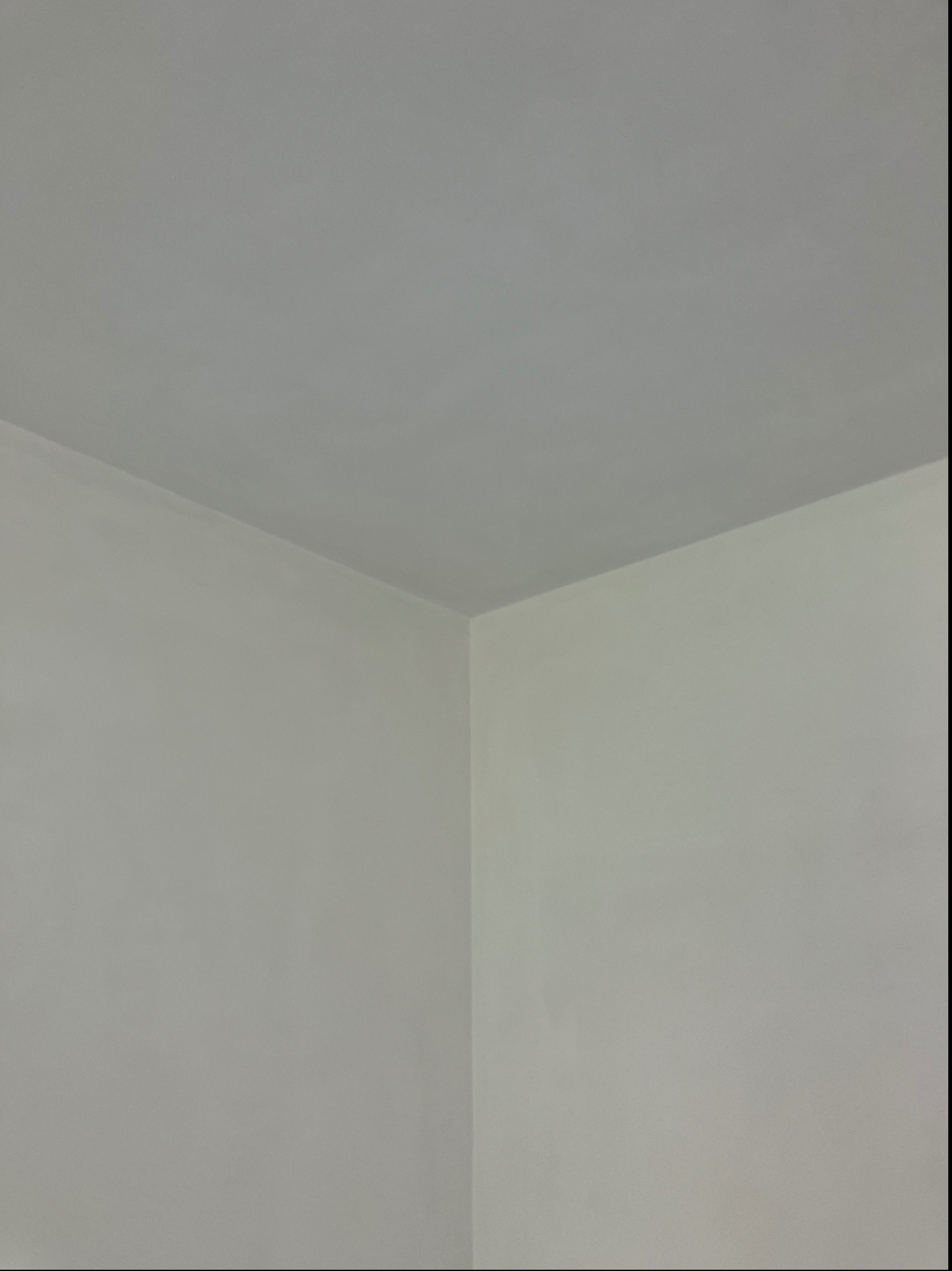 Wewnętrzny narożnik pokoju po zakończonych pracach, ściany i sufit pomalowane na jasny, neutralny odcień szarości, widoczne subtelne różnice w odcieniach na ścianach.