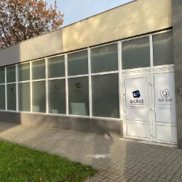 Okna i drzwi biura z naklejonymi logotypami firm Wakkat i SpS Etat, widoczne z zewnątrz na tle chodnika i trawnika.