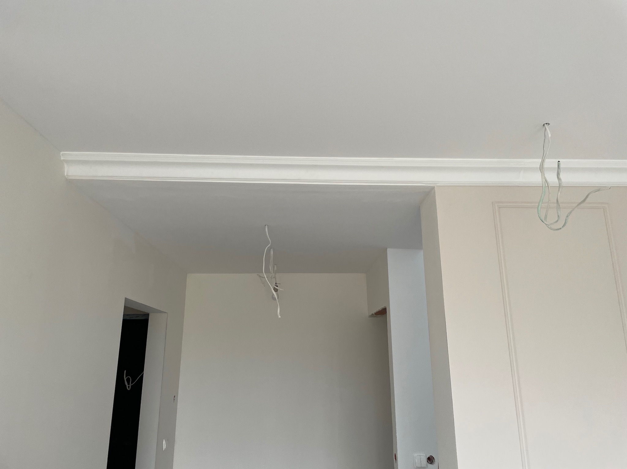 Wnętrze w trakcie remontu z zamontowaną listwą dekoracyjną pod sufitem, widoczne wystające przewody elektryczne i przygotowane ściany pod malowanie.