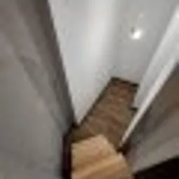 Poddasze z izolacją z wełny mineralnej, widok na schody prowadzące w dół, widoczne białe ściany i drewniana podłoga, oświetlenie punktowe na suficie.