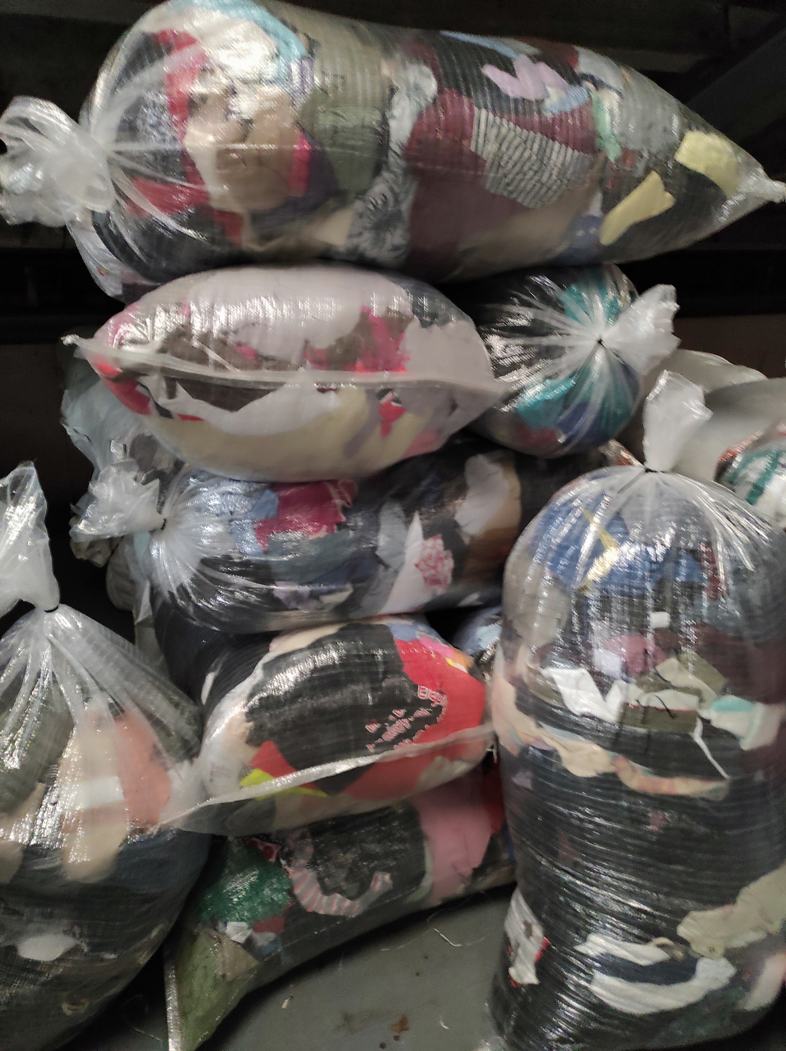 Stos worków foliowych wypełnionych odzieżą używaną, widoczne różne kolory i faktury materiałów.