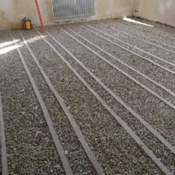 Przygotowanie podłoża pod posadzkę: warstwa drobnego kruszywa z listwami poziomującymi w surowym wnętrzu z odsłoniętą cegłą.