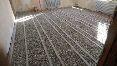 Przygotowanie podłoża pod posadzkę: warstwa drobnego kruszywa z listwami poziomującymi w surowym wnętrzu z odsłoniętą cegłą.