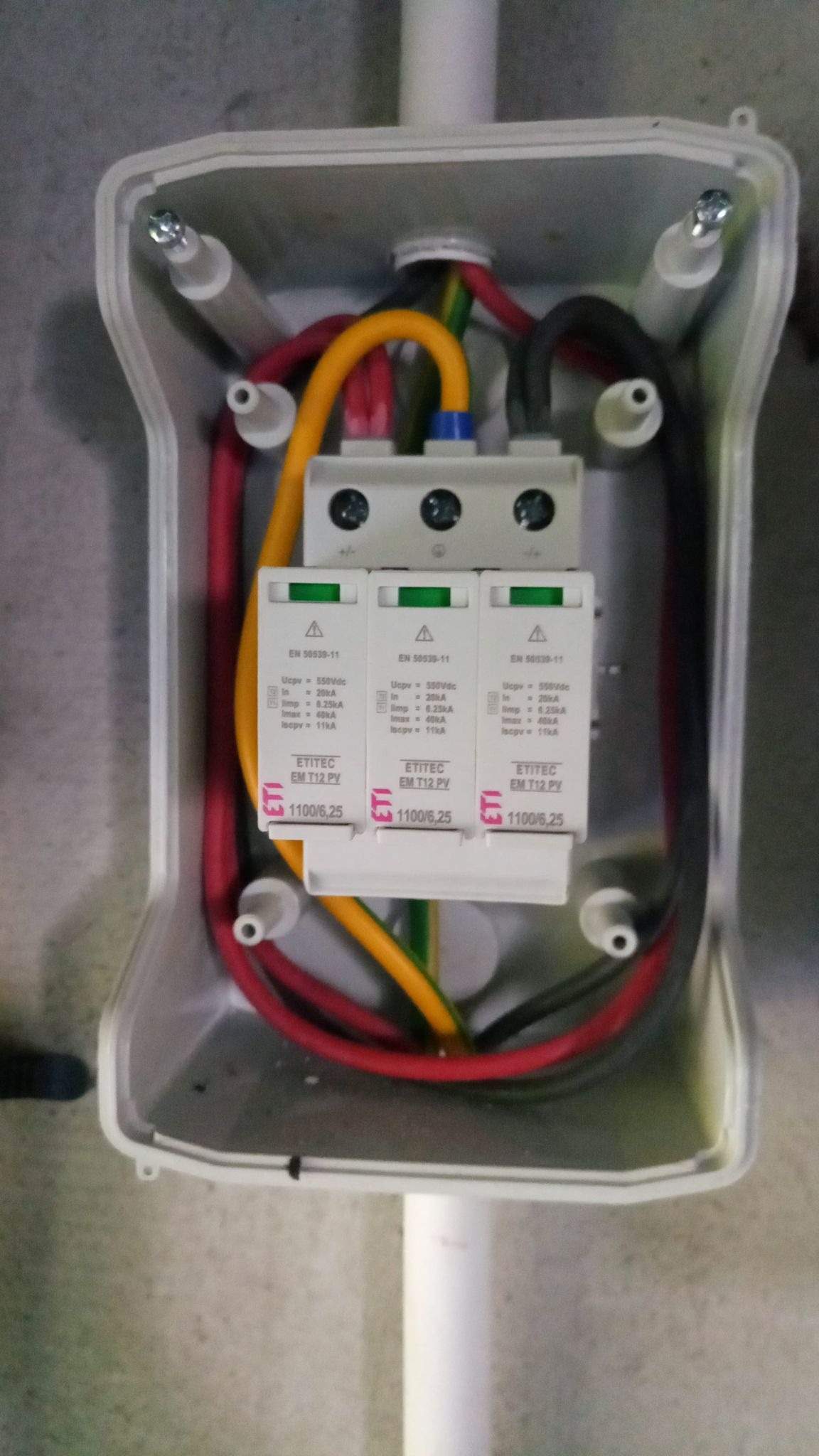 Rozdzielnica z ogranicznikami przepięć ETI do instalacji fotowoltaicznej, widoczne przewody w kolorach czerwonym, żółto-zielonym i czarnym.
