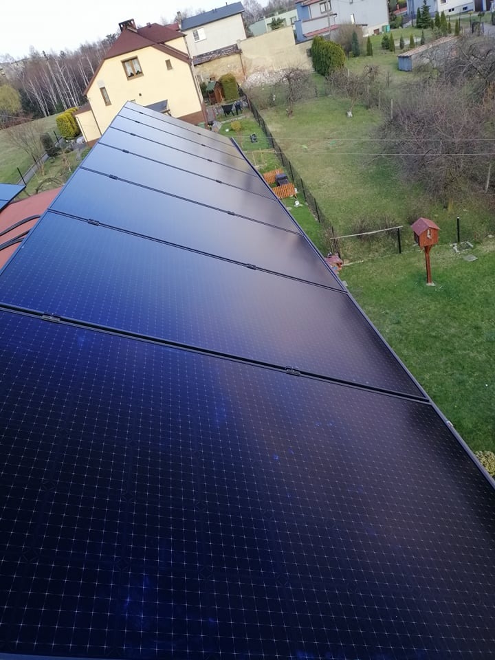 Instalacja paneli słonecznych na dachu domu jednorodzinnego, widok z góry na panele i otaczający ogród z domkami dla ptaków.