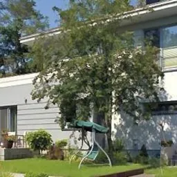 Nowoczesny dom z dwuspadowym dachem, wykończony w odcieniach szarości i bieli, z tarasem i zielonym ogrodem z huśtawką.