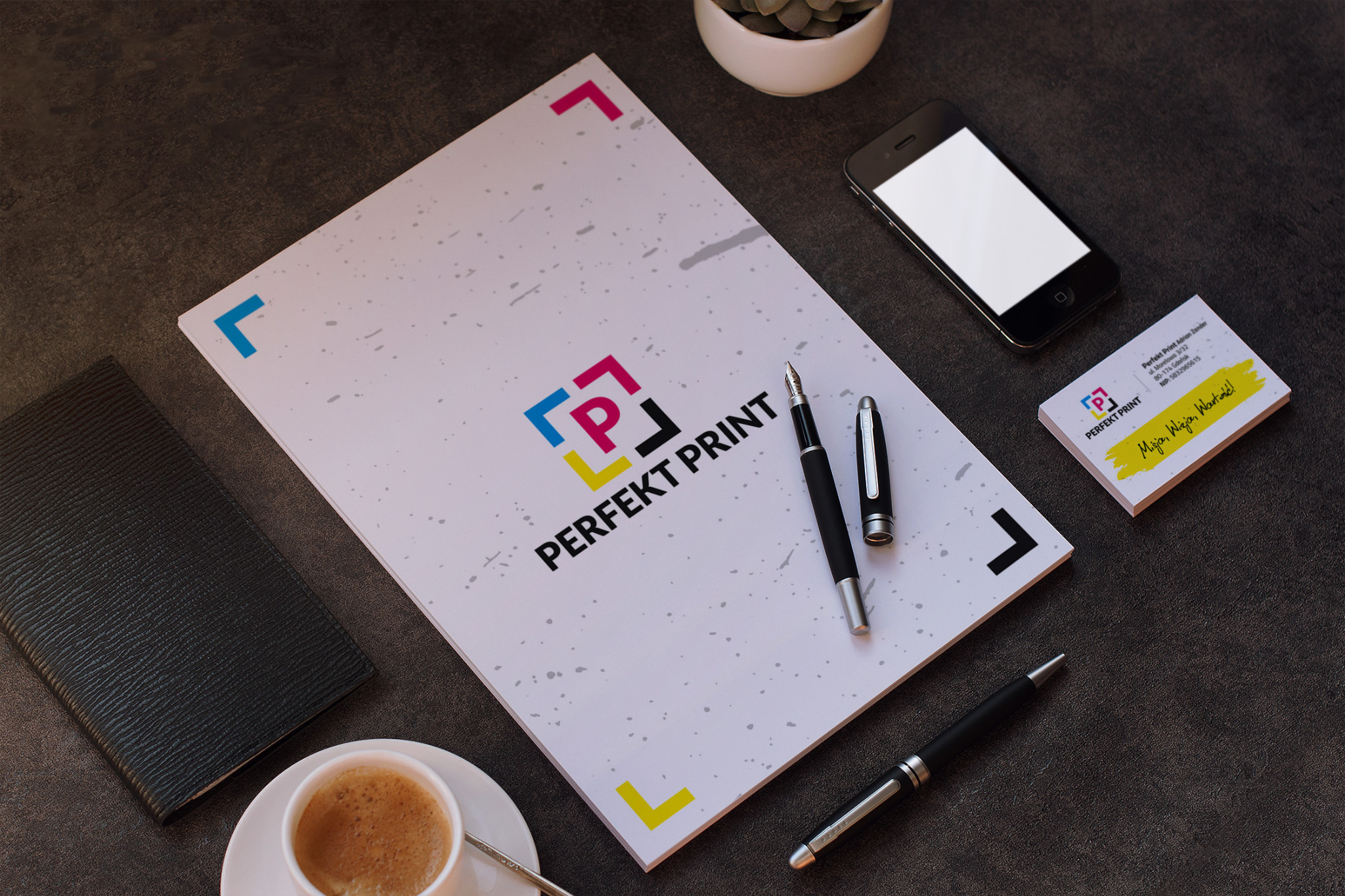 Arkusze papieru z logotypem firmy drukarskiej, wizytówki, telefon, filiżanka kawy i dwa pióra na ciemnym blacie