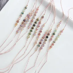 Delikatne bransoletki na sznurku z kolorowymi kamieniami i złotymi koralikami, ułożone równolegle na białym tle.