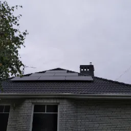 Ciemne panele fotowoltaiczne na grafitowym dachu domu jednorodzinnego z cegły, widok z dołu, pochmurne niebo.