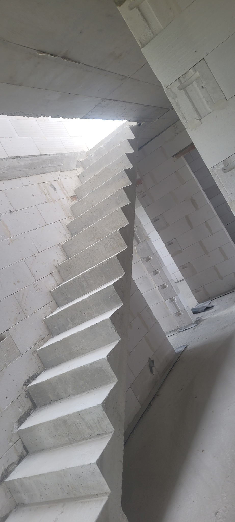 Surowe, betonowe schody w trakcie budowy wewnątrz domu z bloków, widoczne niedoskonałości i brak wykończenia, surowy stan deweloperski.