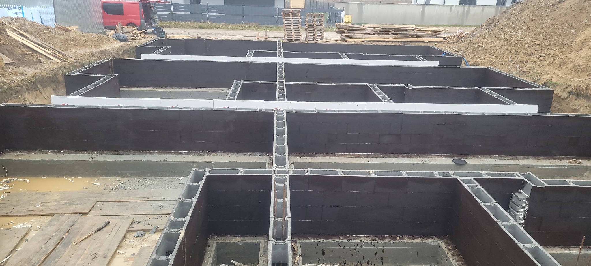 Fundamenty domu z bloczków betonowych zabezpieczone izolacją bitumiczną w Wólce Sokołowskiej, widoczne białe elementy szalunkowe.