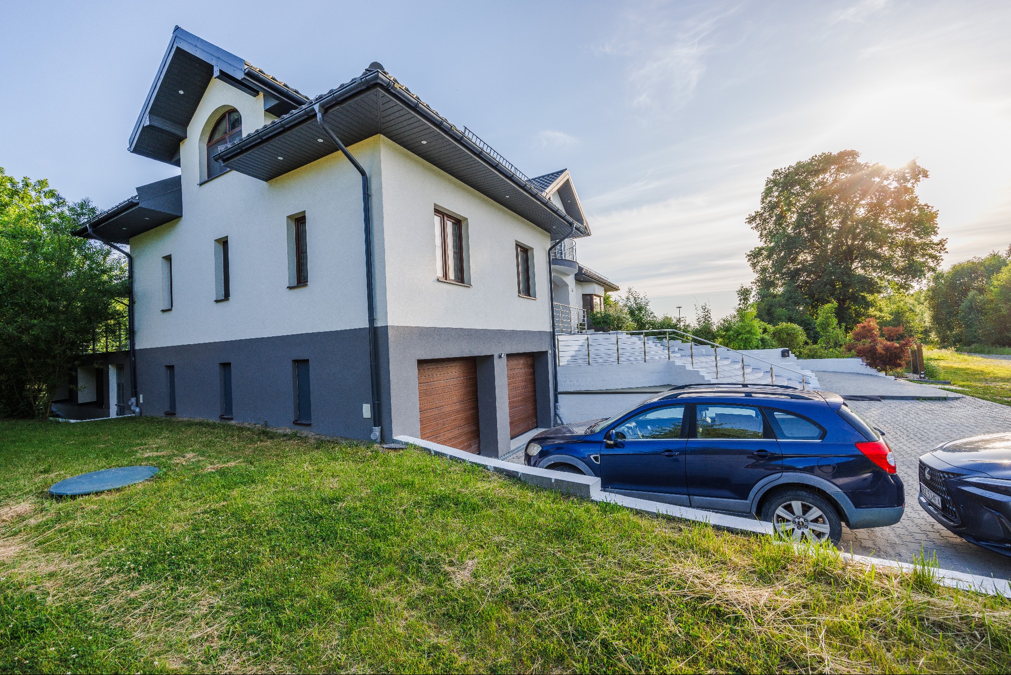 Dwupiętrowy dom z szarym dachem i dwoma samochodami zaparkowanymi na podjeździe, widok z dołu na trawnik