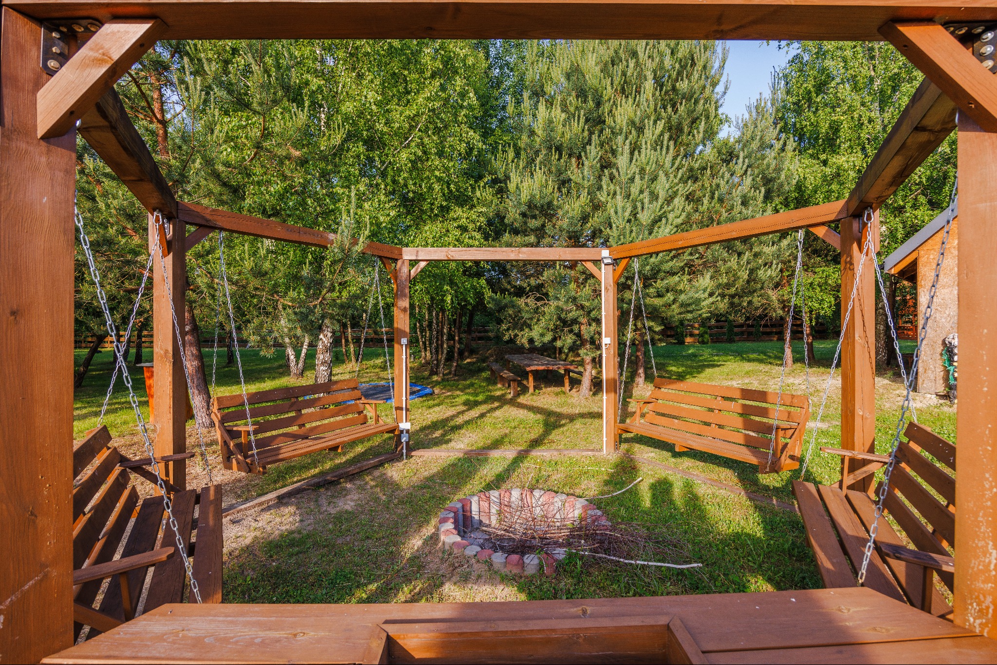Drewniana konstrukcja z huśtawkami, paleniskiem i stołem piknikowym w ogrodzie, widok z perspektywy dolnej ramy konstrukcji.