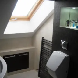 Jasna łazienka na poddaszu z oknem dachowym, grzejnikiem drabinkowym, zabudową pod umywalką i wnęką z półkami na kosmetyki.