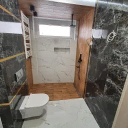 Nowoczesna łazienka z marmurowymi płytkami w odcieniach bieli i szarości, brązowymi akcentami drewna na ścianach i podłodze prysznicowej, podwieszana toaleta, czarna armatura i minimalistyczna...