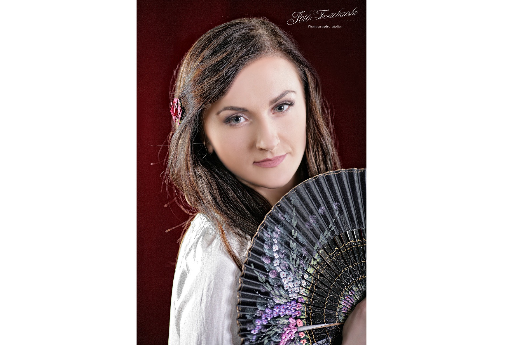 Portret kobiety z wachlarzem i kwiatem we włosach na ciemnoczerwonym tle, w studiu fotograficznym.