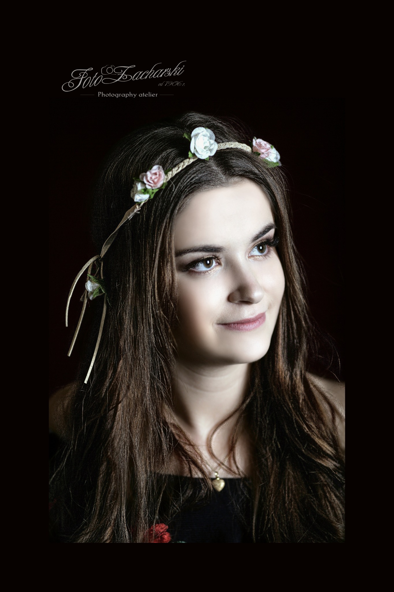 Portret młodej kobiety z wiankiem z kwiatów na głowie, spoglądającej w górę, z delikatnym uśmiechem, na ciemnym tle.