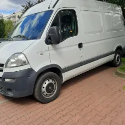 Biały samochód dostawczy Opel Movano zaparkowany na czerwonej kostce brukowej, widok z boku, na oponie widoczne oznaczenia Hankook.