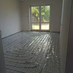 Instalacja ogrzewania podłogowego na siatce w pustym, jasnym pokoju z oknem na zewnątrz.