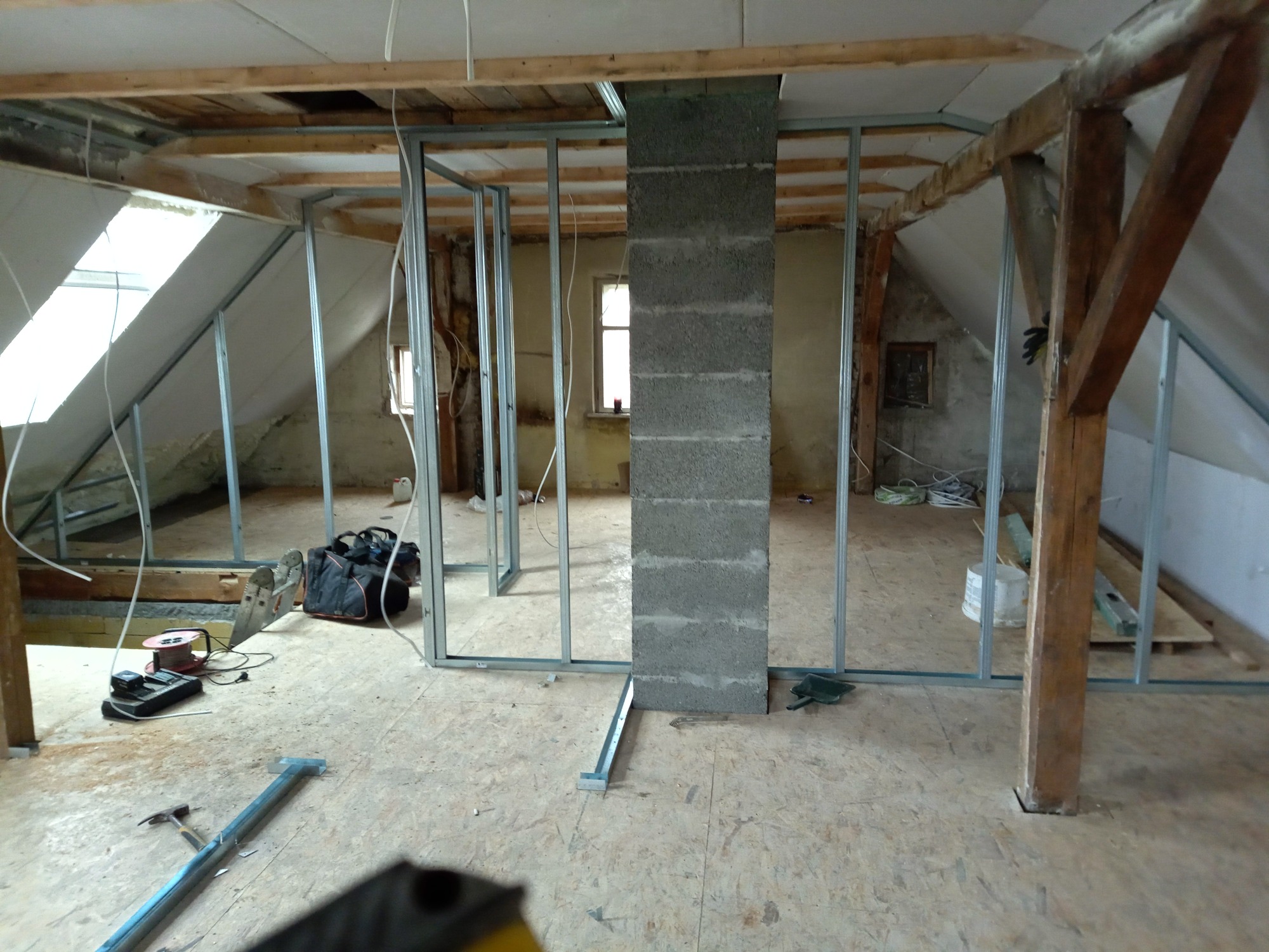 Montaż metalowej konstrukcji ścian działowych na poddaszu w Wydminach, widoczne drewniane elementy konstrukcyjne dachu i narzędzia pracy.