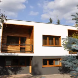 Nowoczesny dom z białymi ścianami, drewnianymi elementami elewacji i szarą podmurówką, częściowo zasłonięty przez świerk kłujący 'Glauca'.