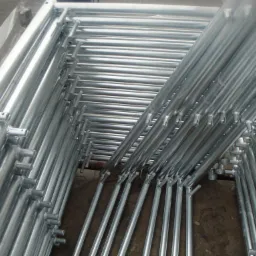 Stos ocynkowanych, stalowych elementów rusztowania elewacyjnego, widoczne spawane złącza i otwory montażowe.