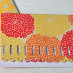Kreatywna, kolorowa kartka z motywem kwiatowym i perforacją na brzegu, obok koperta w żółte serduszka.