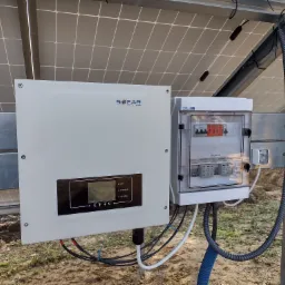 Instalacja fotowoltaiczna: falownik Sofar Solar i skrzynka zabezpieczeń AC/DC zamontowane na konstrukcji wsporczej, widoczne panele fotowoltaiczne w tle, okablowanie w peszlach.