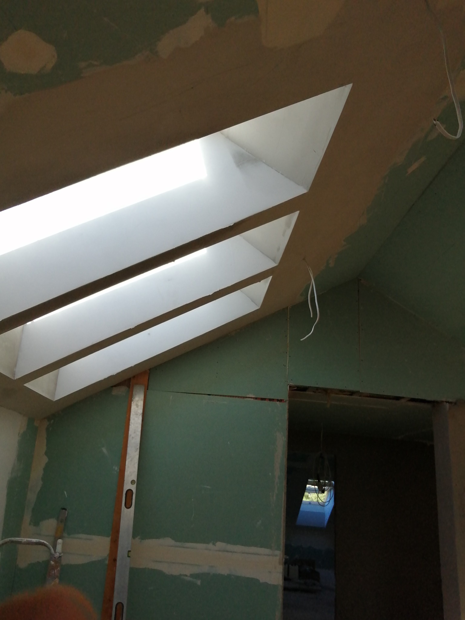 Poddasze w Olsztynie z oknami dachowymi i ścianami pokrytymi płytami gipsowo-kartonowymi przed szpachlowaniem, widoczny poziomica i przewody elektryczne.