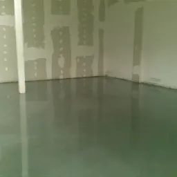 Świeżo wylana, gładka, szara podłoga w pomieszczeniu w trakcie remontu, z widocznymi śladami po łataniu ścian.