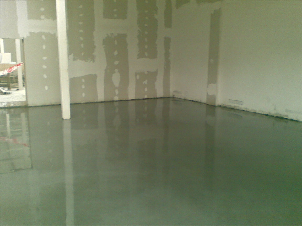 Świeżo wylana, gładka, szara podłoga w pomieszczeniu w trakcie remontu, z widocznymi śladami po łataniu ścian.