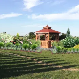 Wizualizacja ogrodu z drewnianą altaną, rabatami kwiatowymi z różami i lawendą oraz różnorodnymi krzewami ozdobnymi na tle zielonego trawnika i błękitnego nieba.