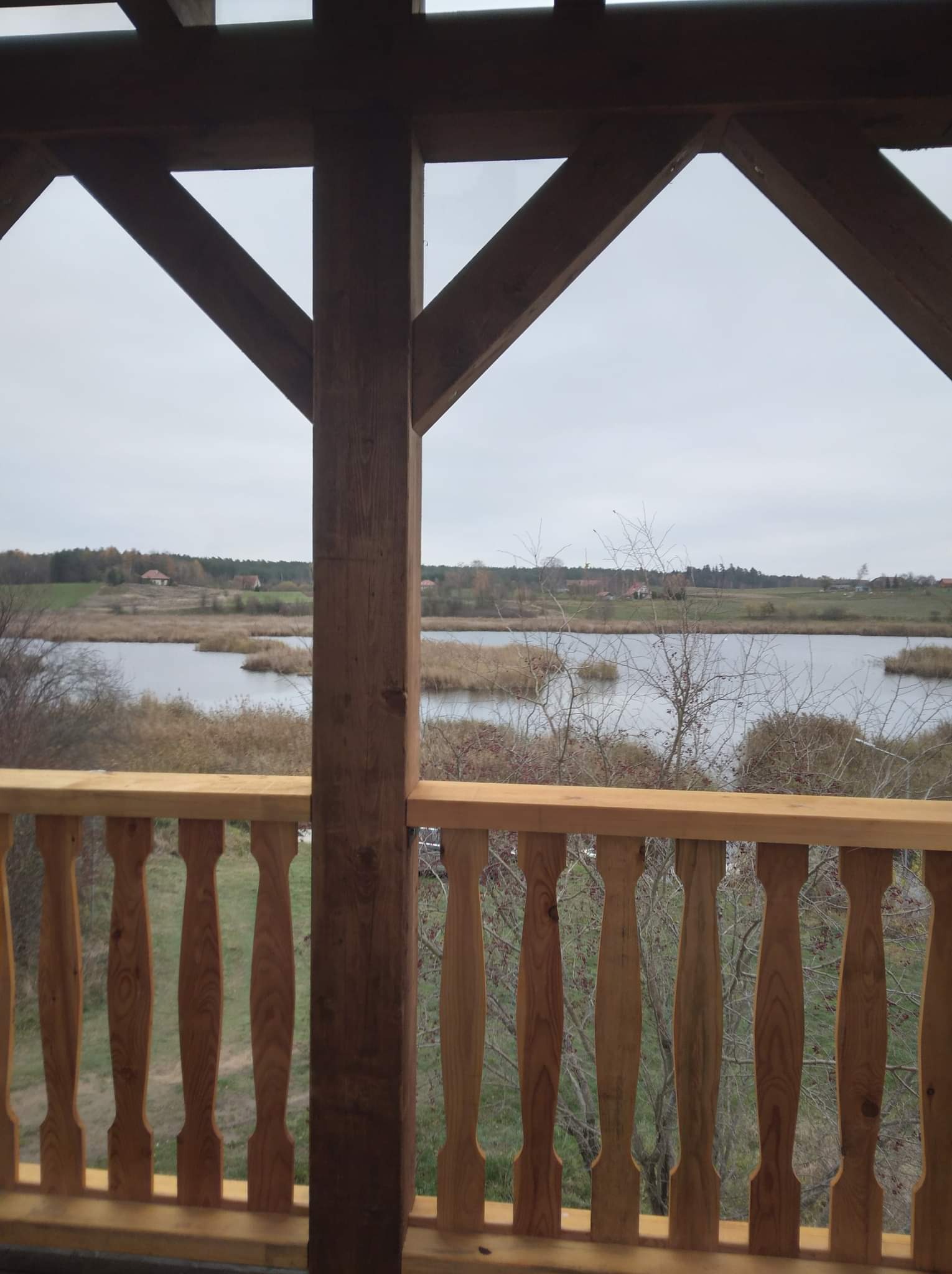 Drewniana balustrada z toczonymi elementami i widokiem na jezioro w pochmurny dzień.