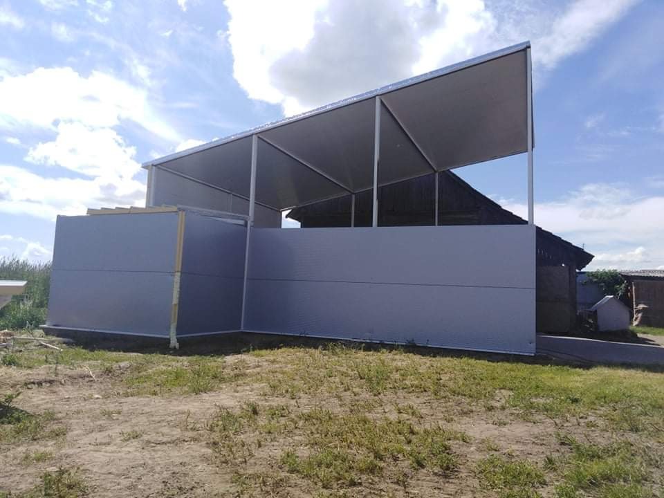 Szkielet konstrukcji hali z szarych paneli, widok z zewnątrz na tle nieba z chmurami.