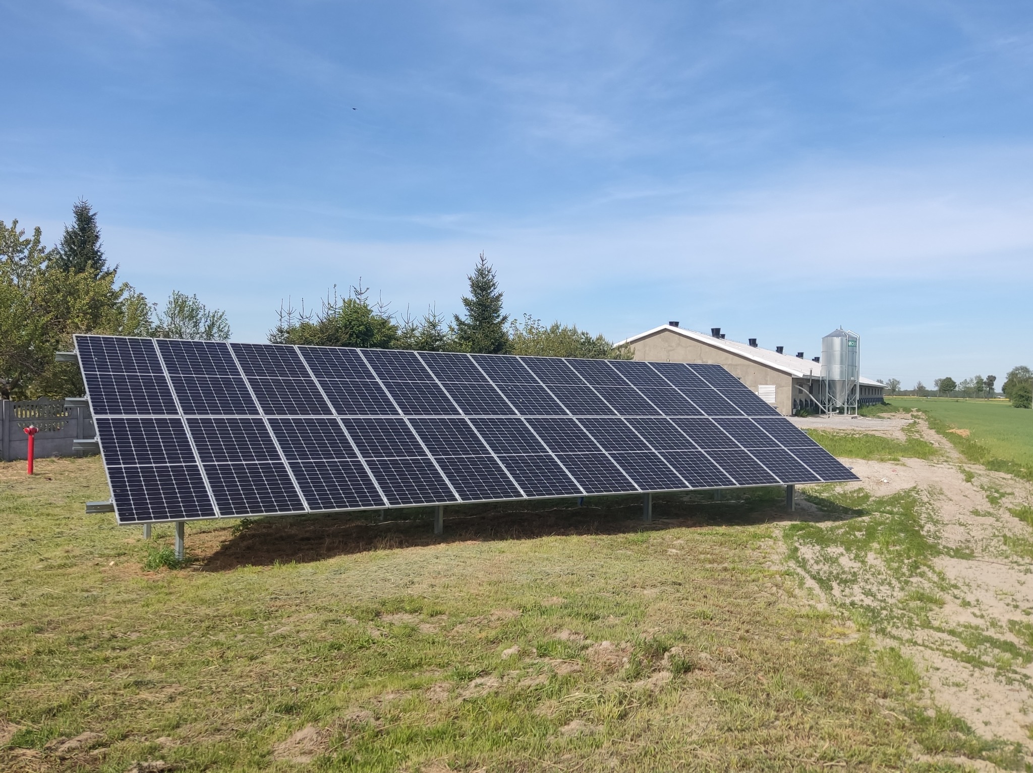 Instalacja paneli słonecznych w okolicy Warszawy, widoczna farma w tle i czerwony hydrant.