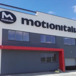 Budynek firmy z dużym logotypem 'motion' w owalu i napisem 'motionitalia' na elewacji w Nowym Sączu, widok z zewnątrz w słoneczny dzień.