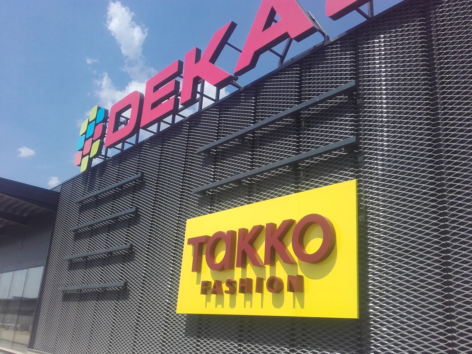 Zewnętrzny szyld sklepu Dekada i Takko Fashion na fasadzie budynku, widok z dołu, z lekkim pochyleniem w lewo.