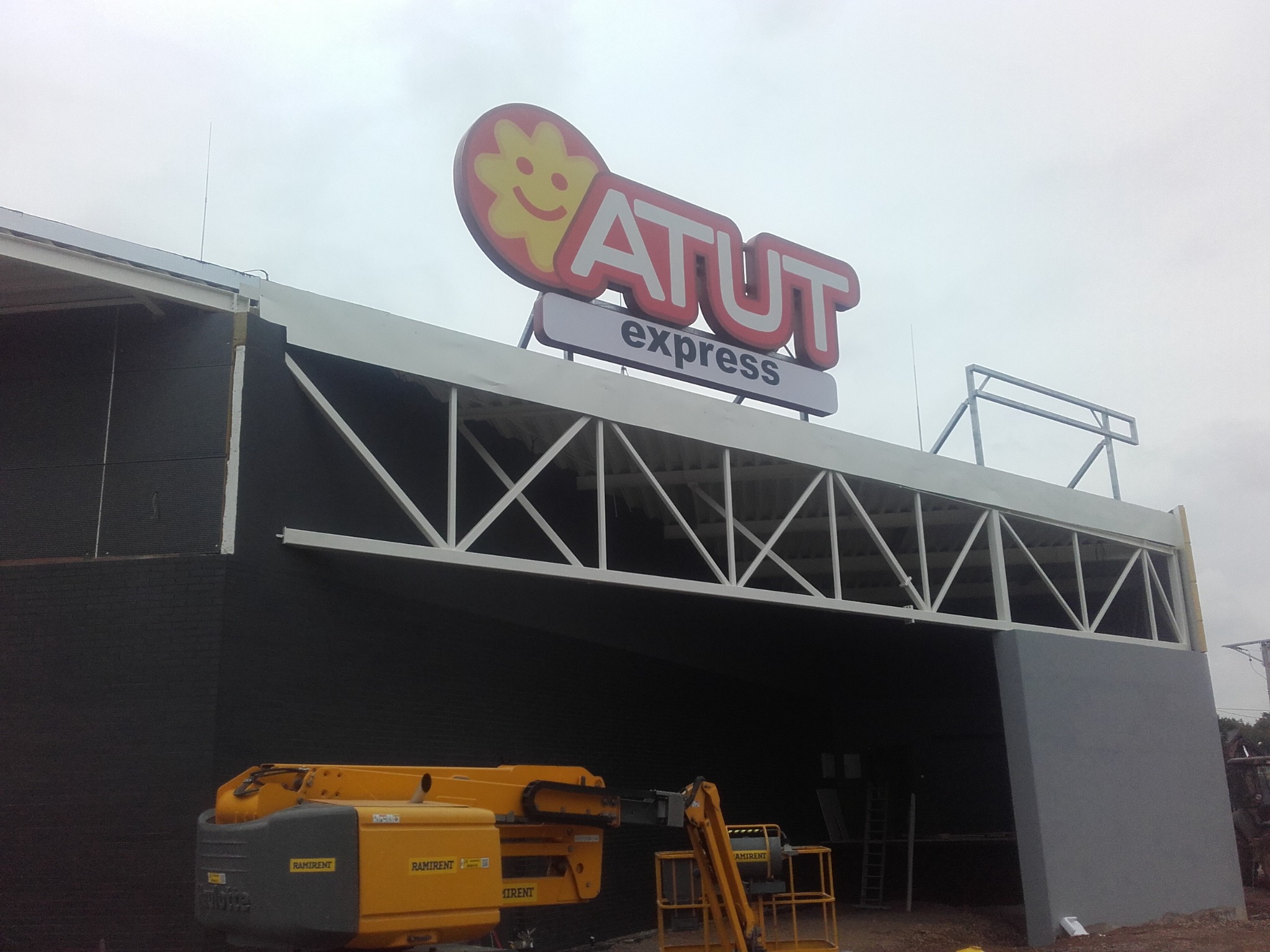 Montaż szyldu ATUT express na budynku, widoczny podnośnik koszowy Ramirent.