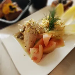 Elegancko podane danie: plasterki kurczaka z kaparami i kiełkami, kremowe puree ziemniaczane z koperkiem, plastry pomidora i cykoria na białym talerzu.