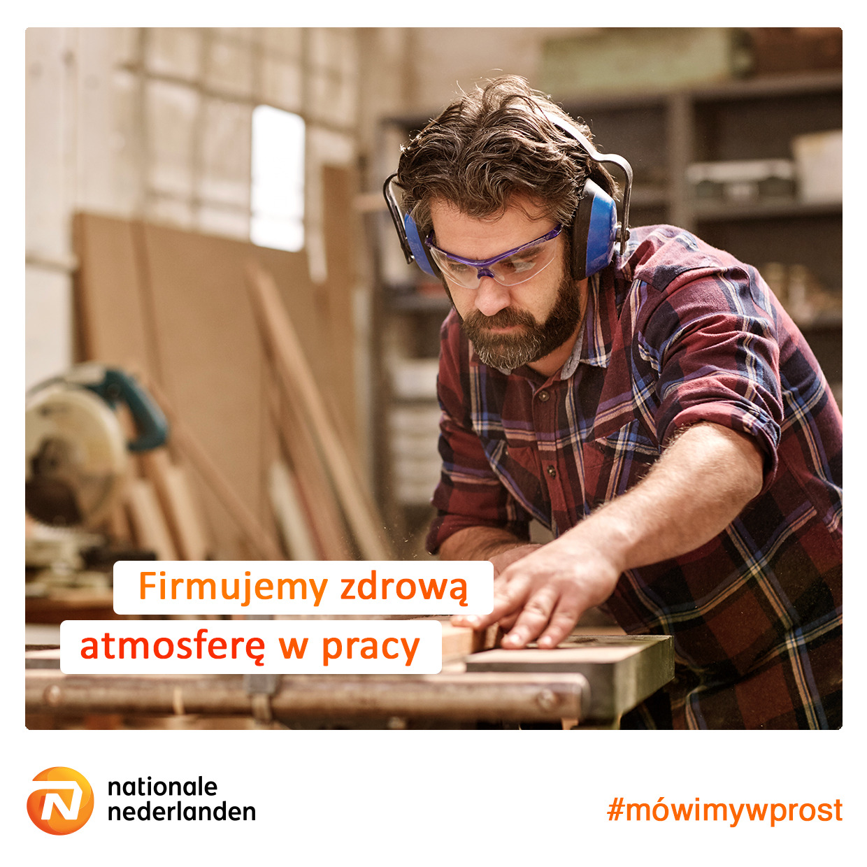 Stolarz w okularach ochronnych i słuchawkach tnący drewno na warsztacie, w tle piła tarczowa i półki z narzędziami, logo Nationale Nederlanden w rogu.
