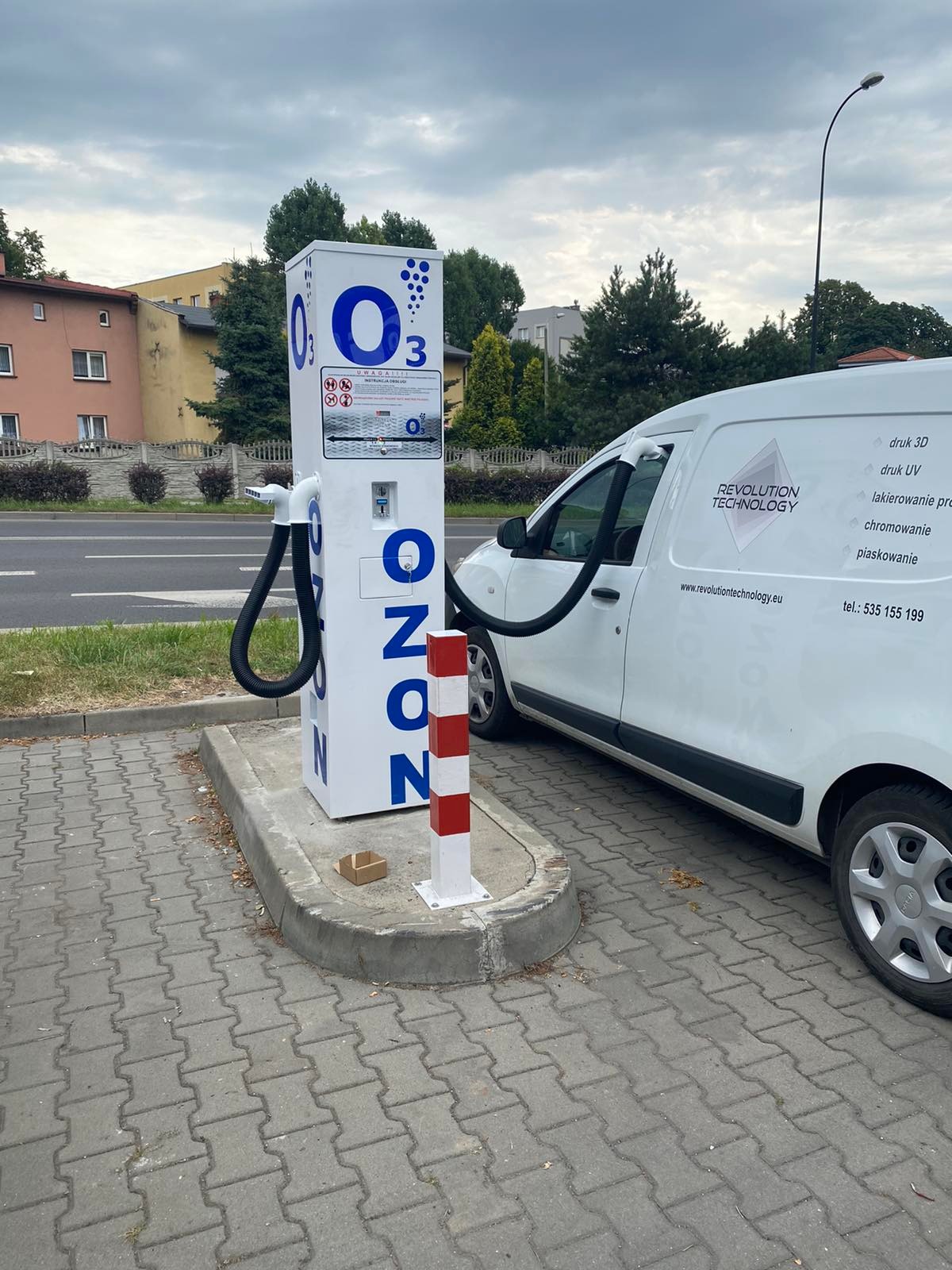 Stanowisko do ozonowania pojazdów z podłączonym wężem do wnętrza białego samochodu dostawczego z logo firmy Revolution Technology na tle ulicy.