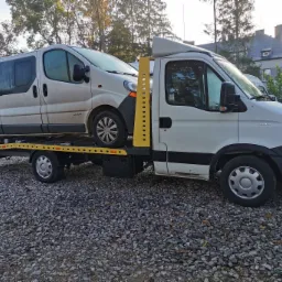 Biała laweta z przewożonym brudnym busem na tle szaro-zielonej scenerii w Grębkowie.