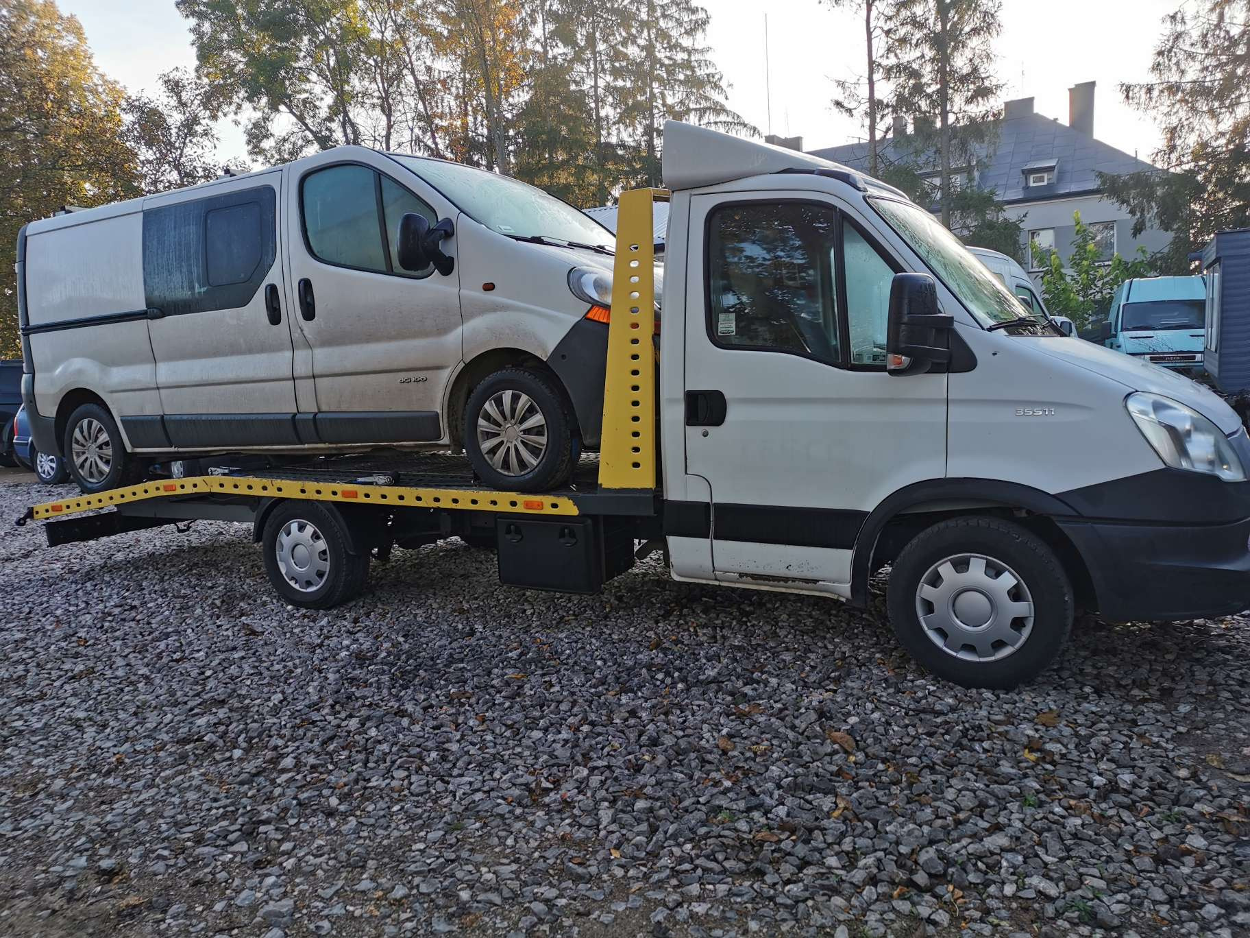Biała laweta z przewożonym brudnym busem na tle szaro-zielonej scenerii w Grębkowie.