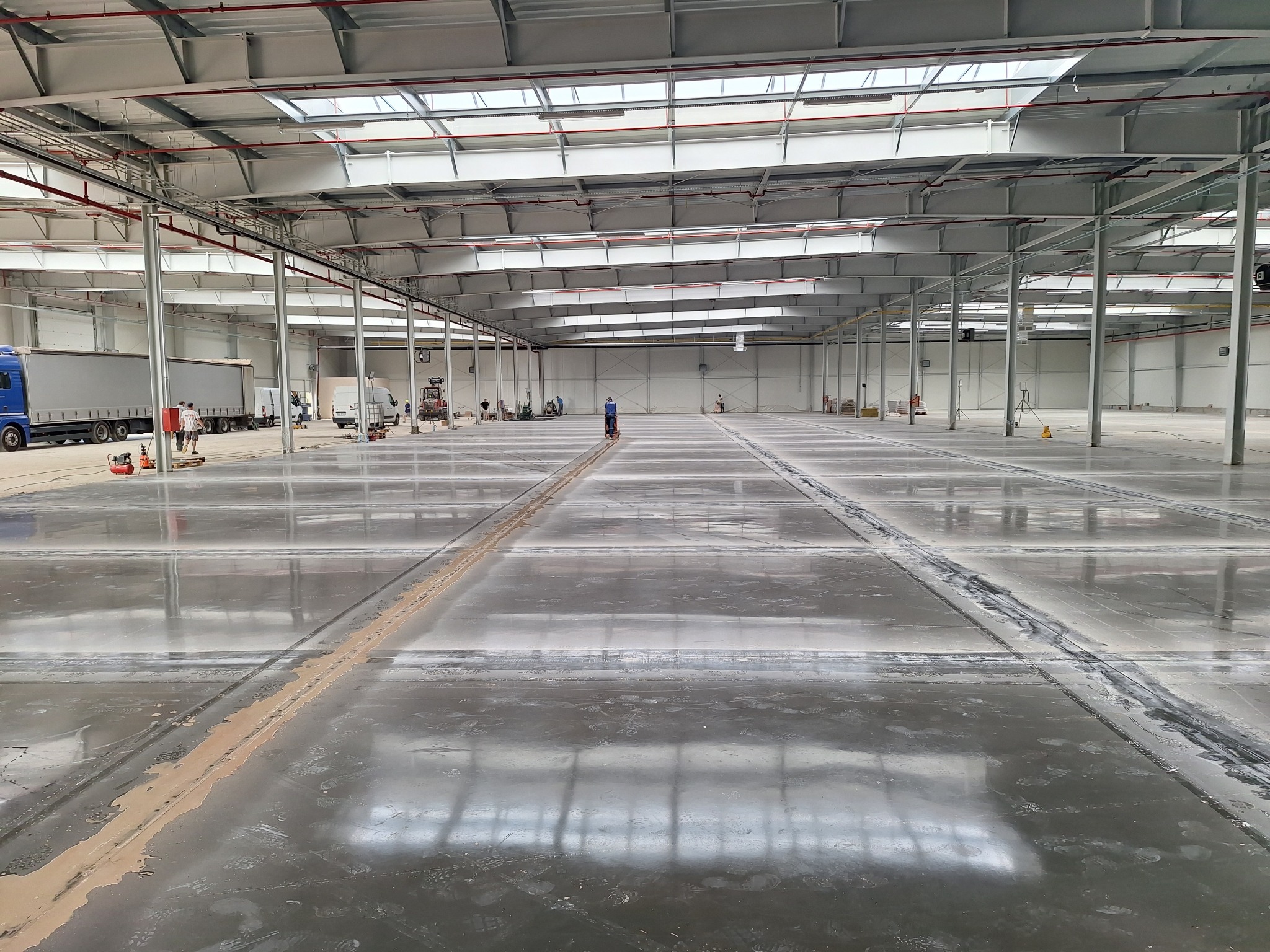 Świeżo wylana posadzka przemysłowa w hali magazynowej, widoczne ślady butów i niedociągnięcia wzdłuż dylatacji.