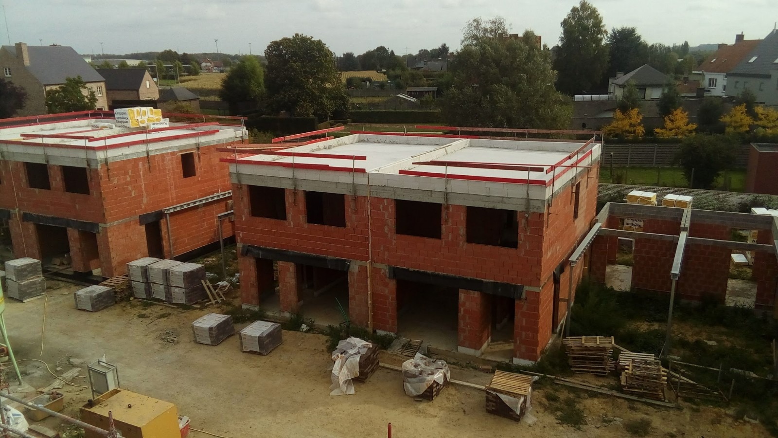 Wznoszenie ścian dwukondygnacyjnych domów z czerwonej cegły na osiedlu, widok z góry, materiały budowlane na paletach w pobliżu.