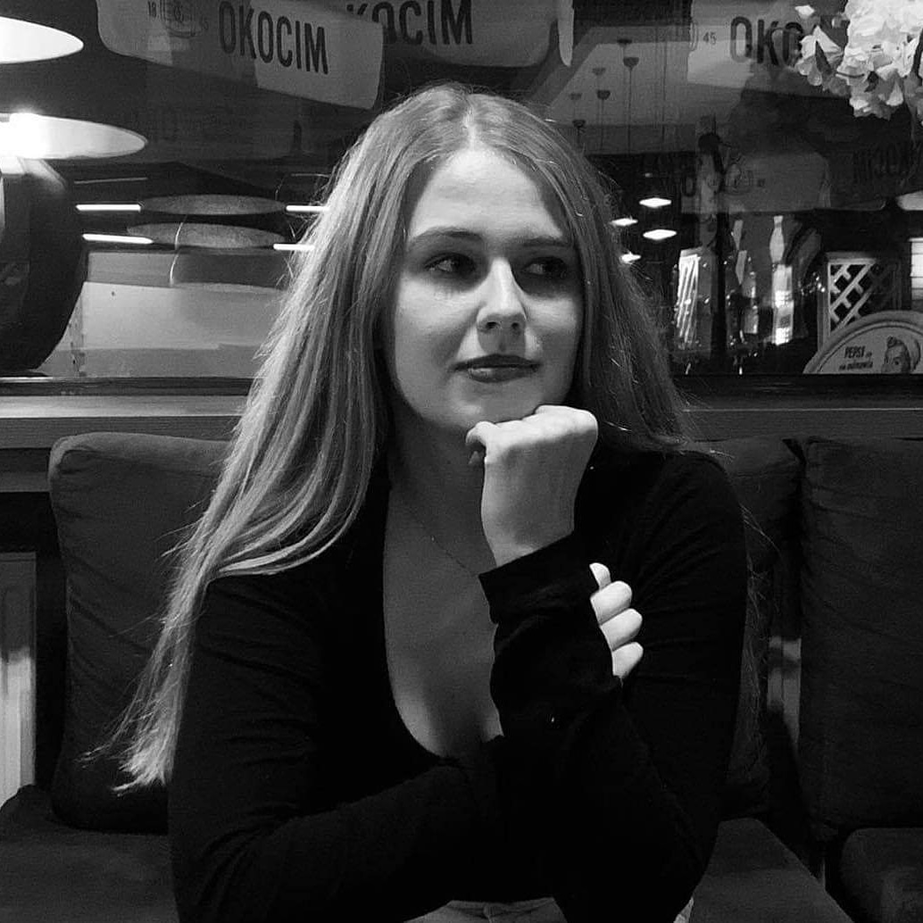 Portret kobiety o długich blond włosach, oparta broda na dłoni, w tle reklamy piwa Okocim w kawiarni.