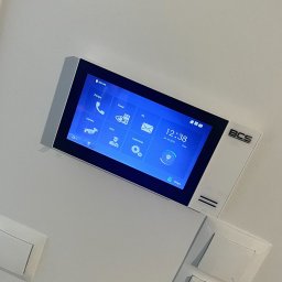 JLN Technology Systems Dariusz Zbigniew Urbański - Panel dotykowy wideodomofonu BCS zamontowany na białej ścianie, widoczny ekran z ikonami i datą 24-10-2022, obok włączniki światła.