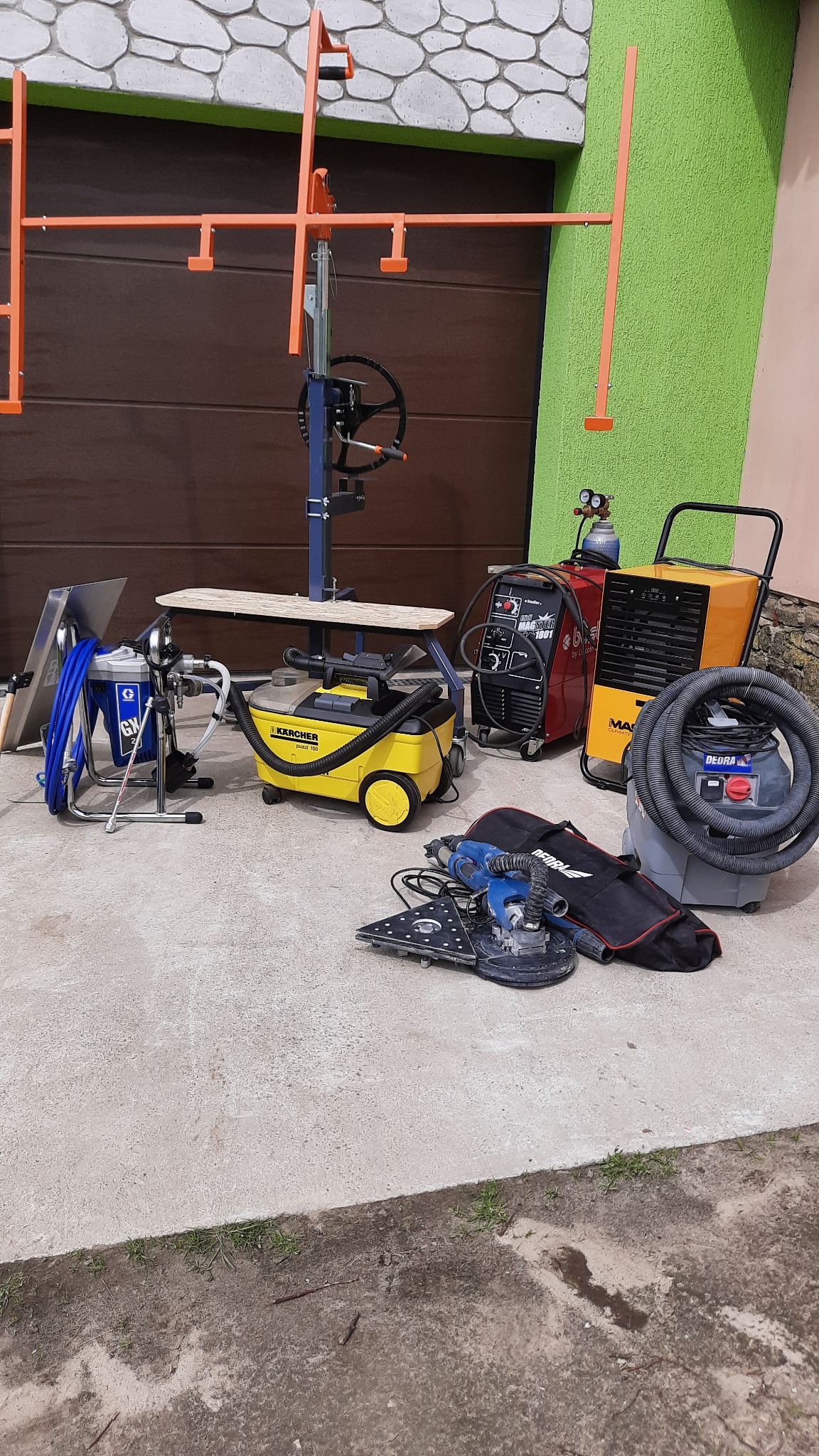 Zestaw narzędzi budowlanych: podnośnik do płyt gipsowo-kartonowych, agregat malarski, odkurzacz przemysłowy Karcher, spawarka, nagrzewnica oraz szlifierka do gipsu DeWalt z workiem, na betonowej...