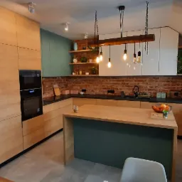 Nowoczesna kuchnia z wyspą, drewnianymi frontami, ceglaną ścianą i wiszącymi lampami z żarówkami Edisona.